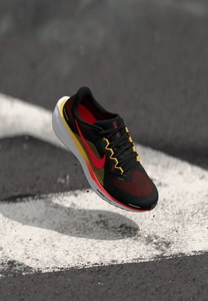 Black and red athletic shoe with a mesh design, accented by yellow stripes and a white sole, featuring black laces and visible branding.
