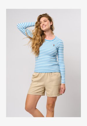 Randig långärmad topp i ljusblått och vitt med ribbad textur; har en liten broderad design. Matchad med beige shorts.