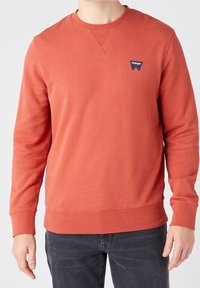 Rode trui met lange mouwen, ronde hals en een klein blauw Wrangler-logo op de linkerborst. Zachte, gladde textuur. Casual pasvorm.