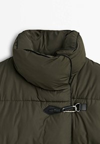 Olijfgroene pufferjack met een hoge kraag, voorzien van zwarte accenten en een voorkant met een togg sluiting. Soepele textuur met gestikte secties.