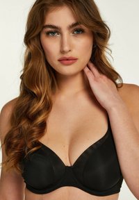 Zwarte onderwired bra met gewatteerde cups met een gladde afwerking en transparante mesh details langs de randen, ontworpen voor ondersteuning en vorm.