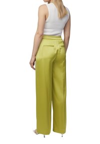 Zielone satynowe spodnie o szerokich nogawkach z elastycznym pasem i dwoma tylnymi kieszeniami. Modelka ma na sobie białą, prążkowaną bluzkę bez rękawów oraz sandały na obcasie.