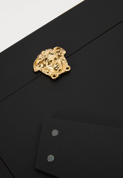 Czarny dodatek z złotym emblematem Meduzy, gładką fakturą oraz metalowymi elementami z nitami, podkreślającymi detale jego designu.