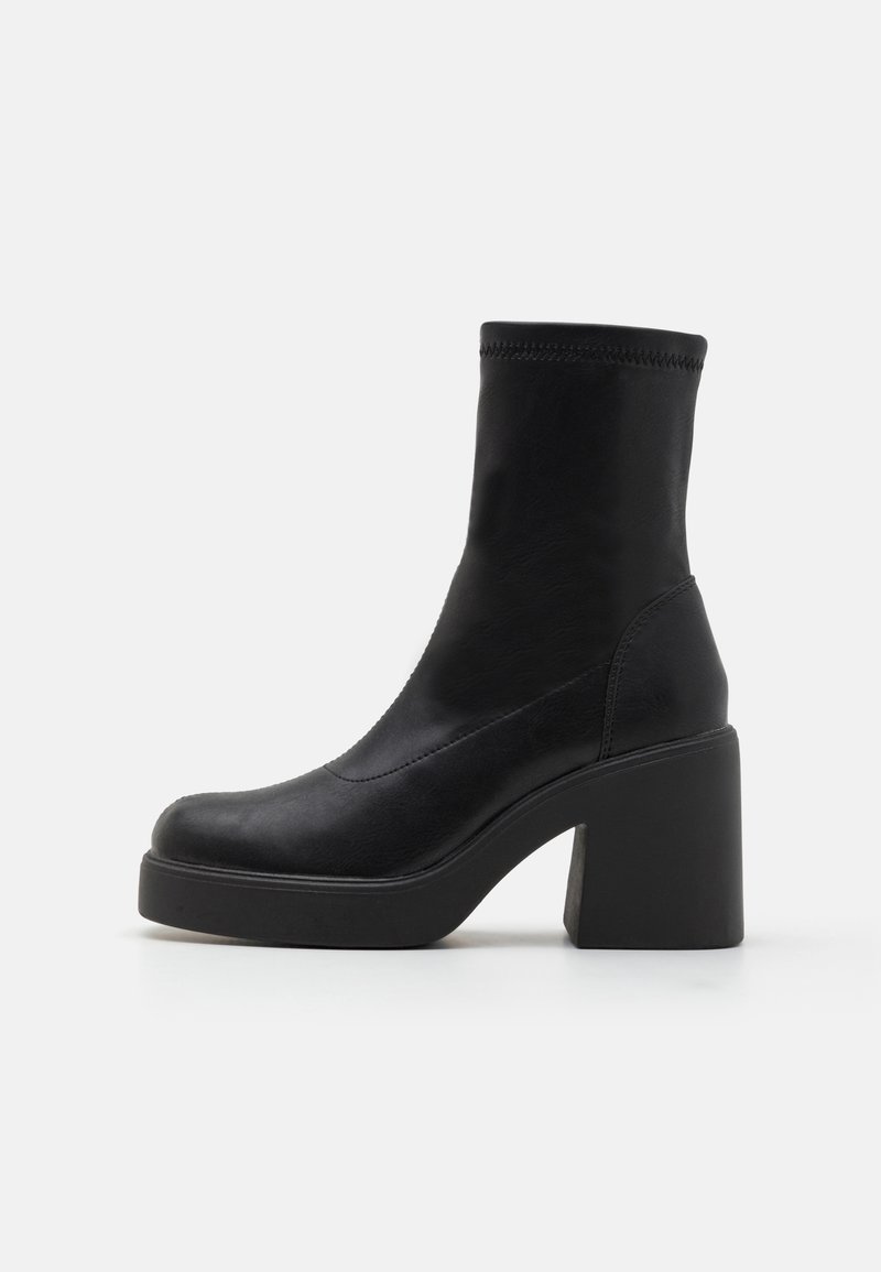 Bottine noire à talon haut épais et plateforme, texture lisse, avec une tige ajustée s'étendant au-dessus de la cheville.