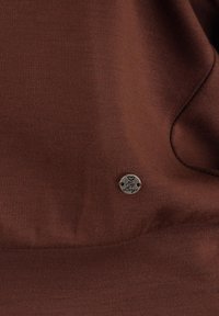Bruine stof met een gladde textuur en een klein metalen embleem met de tekst "Love" en "Lounge" eraan bevestigd. Het ontwerp benadrukt eenvoudige elegantie.