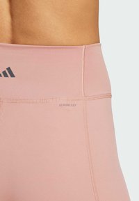 Roze tajice visoki pojas, napravljene od glatkog materijala, s logotipom i otisnutim natpisom "AEROREADY", uz kontrastne šavove.