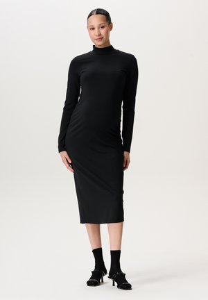 Schwarzes, langärmliges Midikleid mit hohem Kragen, aus glattem Stoff gefertigt. Hat eine figurbetonte Silhouette und wird mit schwarzen Socken und Schuhen mit Absätzen getragen.