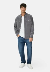 Graues Cordhemd mit zwei Brusttaschen, über einem weißen T-Shirt getragen, kombiniert mit blauen Jeans und weißen Turnschuhen. Glatte Textur.