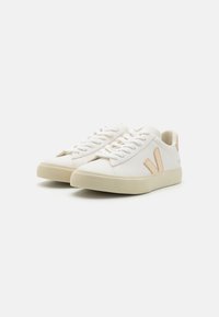 Hvite sneakers med en glatt læroverdel, teksturert gummisåle, med en beige logoakcent og flate lisser. Minimalistisk design.