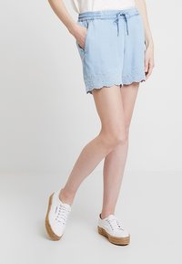 Shorts bleu clair avec une taille élastique, un cordon de serrage noué, des poches avant et un ourlet festonné orné de détails en dentelle œillet.