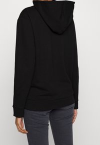 Zwarte hoodie met een zachte textuur, lange mouwen en geribbelde manchetten. Heeft een kangoeroezak en is uitgevoerd in een losse pasvorm.