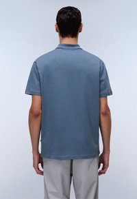 Kurzärmliges Polo-Shirt aus einem gedeckten blauen Stoff, mit klassischem Kragen und geradem Saum, von hinten präsentiert, mit minimalen Nähdetails.