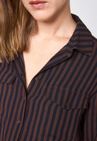 Camicia a righe marroni e blu navy con bottoni, realizzata in tessuto a trama liscia, con collo e una tasca sul petto.