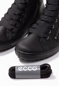 Paire de baskets montantes noires avec de gros lacets noirs et un jeu supplémentaire de lacets enroulés étiqueté ECCO sur fond blanc.