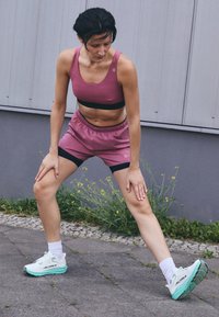  roosa spordirinnahoidja musta paelaga, kokku sobivad roosad lühikesed püksid musta äärisega ja valged spordijalatsid akva sinise tallaga; välinna keskkond.