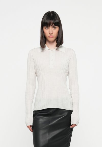 Polo en maille beige clair à manches longues avec un col doux et des boutons, associé à une jupe en cuir noir. Texture lisse, design ajusté.