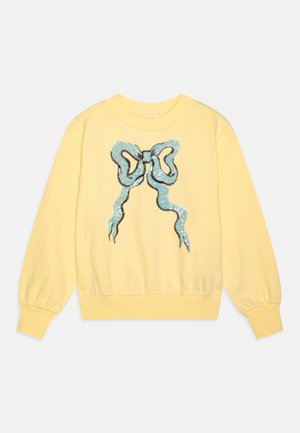 Sweat-shirt jaune à manches longues avec poignets et ourlet côtelés, présentant un grand nœud en sequins bleus sur le devant.