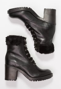 Botas de cuero negro con un puño de piel sintética negra acolchado, punta redonda, cordones en la parte delantera y tacón grueso. Suela de goma con relieve para mayor agarre.