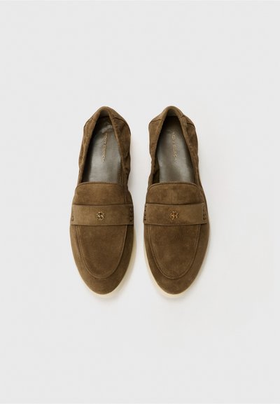 Braune Wildleder-Slipper mit runder Zehenpartie, dekorativem Band und goldfarbenem Logo-Detail. Weiche Textur und lässiges Design.
