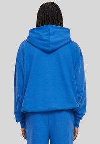 Sudadera azul oversize con capucha, que presenta una textura suave, mangas largas y puños acanalados, combinada con joggers a juego.