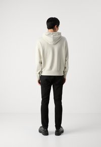 Sudadera con capucha de color gris claro y corte relajado, con dobladillo acanalado y mangas con puños. Combinada con pantalones negros ajustados y zapatos negros.