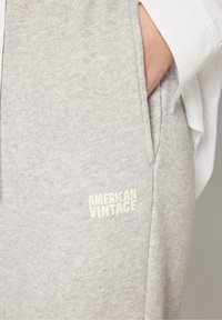 Pantalon de survêtement en coton gris avec une surface texturée, doté d'une poche latérale et d'un logo "AMERICAN VINTAGE" en relief de couleur claire.
