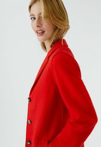 Red wool blazer with a structured design, notched lapels, and three buttons. Features pockets and a textured finish.