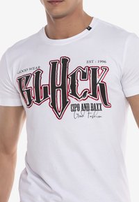 Weißes kurzärmeliges T-Shirt aus Baumwolle mit kräftigem schwarzen und roten grafischen Text, der den Markennamen und das Gründungsjahr zeigt, einfacher runder Ausschnitt.