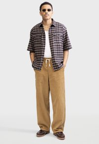Cămașă cu mânecă scurtă în carouri Navy și bej, asortată cu pantaloni din bumbac corduroy bej și pantofi maro. Include buzunare frontale și talie cu șnur.