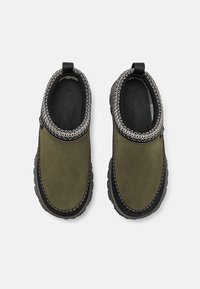 Zöld velúr felsőrésszel, fekete gumi talppal és díszes szürke szemléjű varrással a nyak körül készült slip-on cipők. Texturált bélés és húzófül.