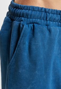 Blue sweatpants with a soft, textured fabric, featuring an elastic waistband and side pockets. The design includes subtle fading for depth.