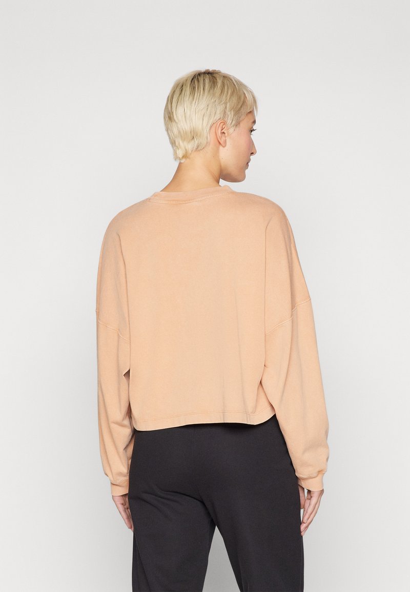Skrócony, długi rękaw sweatshirt z miękkiego materiału w odcieniu brzoskwiniowym. Posiada luźny krój, okrągły dekolt i widoczne detale szwów.