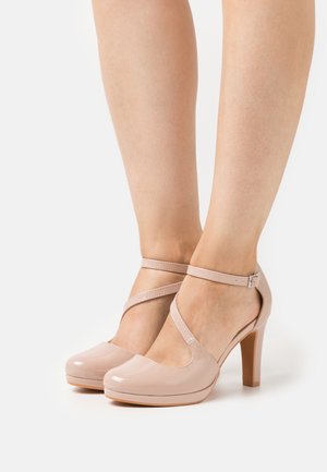 Jasnoróżowe lakierowane szpilki z paskiem wokół kostki i skrzyżowanym wzorem. Charakteryzują się zaokrąglonym noskiem i umiarkowanie wysokim, blokowym obcasem.