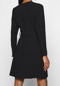 Černé šaty s dlouhými rukávy, přiléhavým korzetem a rozšířenou sukní. Obsahují odpovídající pásek v pase a jsou vyrobeny z hladké tkaniny.