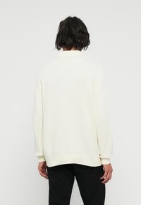 Cremefarbener Strickpullover mit Kragen, weiten Rippbündchen und Saum. Das Design ist lässig geschnitten und hat eine glatte Textur.