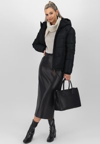 Giacca a vento nera, maglione crema, gonna in pelle nera e stivaletti. Gli accessori includono una borsa strutturata nera. Texture lisce in tutta la composizione.