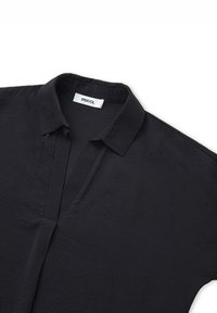 Maglietta nera a maniche corte con colletto a bottoni e una trama sottile. Presenta una placca per un aspetto curato. Etichetta visibile all'interno del colletto.