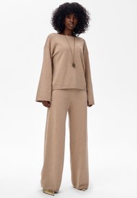 Beżowy zestaw dzianinowy do noszenia na co dzień, składający się z luźnego swetra o szerokich rękawach oraz pasujących szerokich spodni, oba z delikatnym połyskiem.