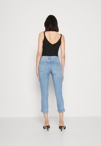 Top de tirantes negro en V combinado con unos pantalones vaqueros cortos de un azul claro. Los jeans tienen un diseño ajustado y bolsillos traseros, con un acabado sin dobladillo.