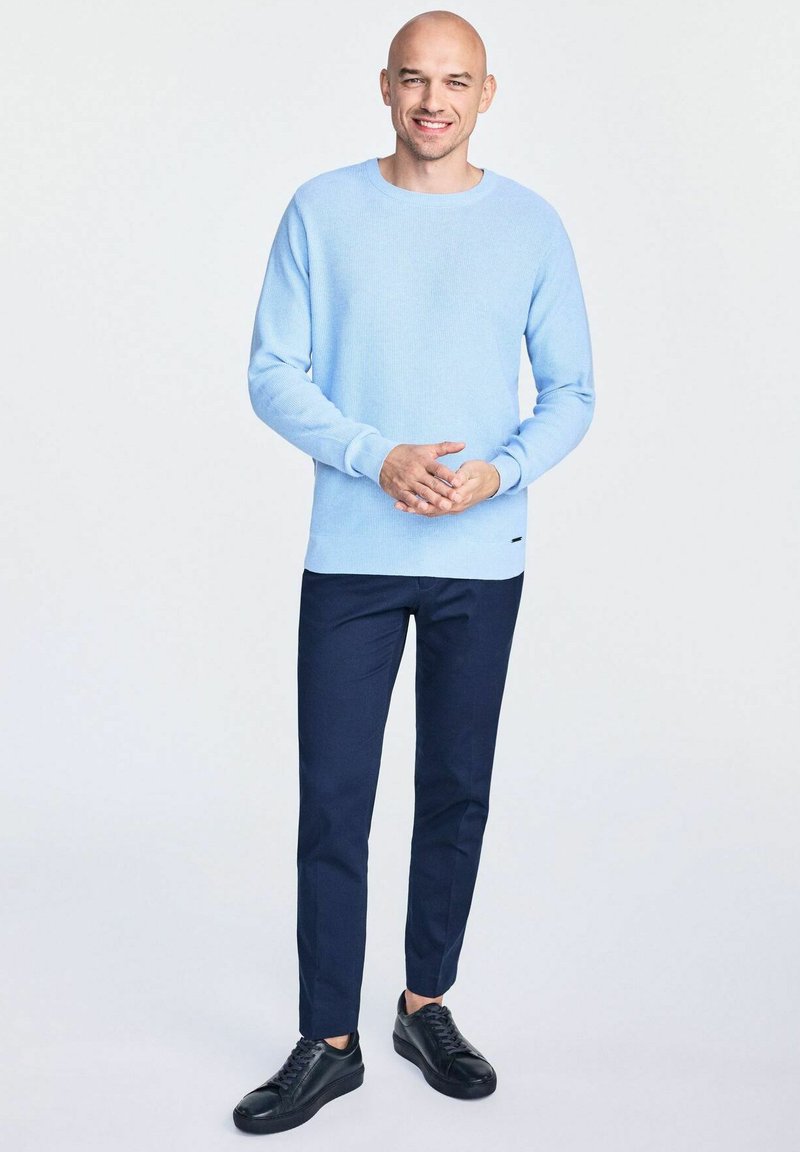 Helles blaues Strickpullover, navyfarbene Slim-Fit-Hosen und schwarze Sneakers. Der Pullover hat einen runden Halsauschnitt und gerippte Bündchen, was einen strukturierten Look erzeugt.