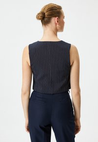 Marineblaue ärmellose Bluse mit weißen Streifen; glattes Material; runder Ausschnitt; kombiniert mit marineblauen Hosen mit Gesäßtaschen und taillierter Passform.