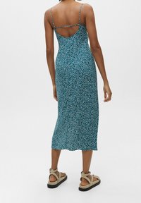 Vestido midi floral en tono verde azulado, con tirantes finos, espalda descubierta y una silueta fluida. La textura parece suave, con un patrón blanco disperso.