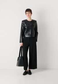 Black leather cropped jacket with round buttons and flap pockets, paired with wide black trousers and a black shoulder bag. Textured loafers complete the look.