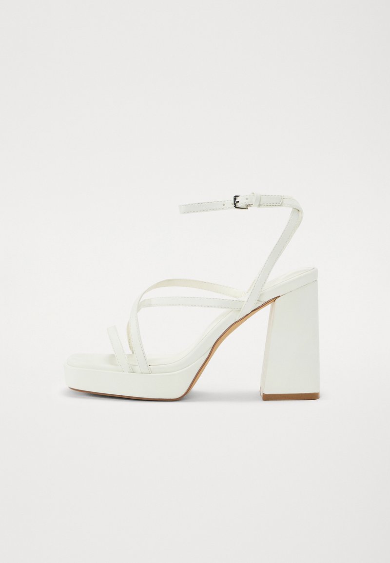Witte platformsandalen met een brede blokhak, voorzien van meerdere dunne bandjes en een verstelbaar enkelbandje. Gladde synthetische materialen.