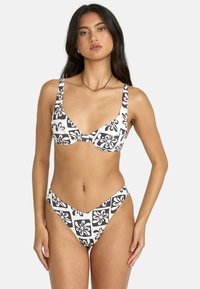 Bikini in bianco e nero con motivo, caratterizzato da una scollatura profonda e spalline larghe sulla parte superiore, completato da un fondo a taglio alto con copertura minima.