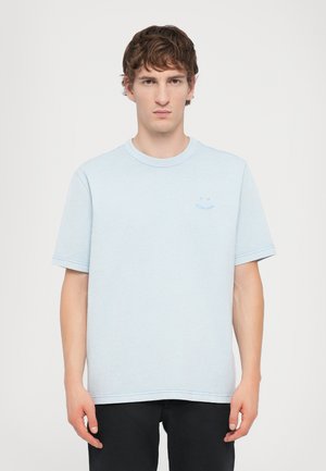 Light blue short-sleeve t-shirt with a round neck, featuring subtle stitching details and a small logo on the left chest. Soft fabric texture.