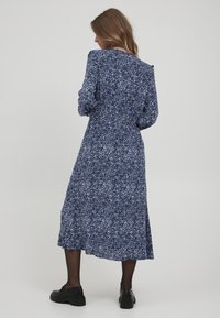 Robe midi à motifs bleu marine avec des manches longues, une silhouette fluide et un ourlet festonné. Associée à des chaussures noires.