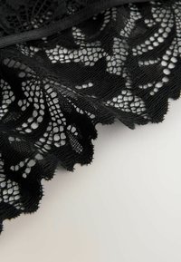 Czarna koronkowa lamówka z misternymi kwiatowymi wzorami, falistymi krawędziami i delikatną, przezroczystą fakturą. Miękka w dotyku na jasnym tle.