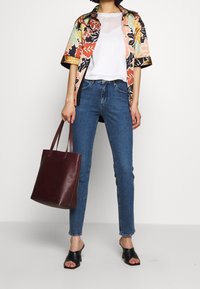 Blommig kortärmad skjorta i svart, orange, grönt och rosa; vit genomskinlig topp; blå åtsittande jeans; vinröd tote-väska; svarta sandaletter med öppen tå.