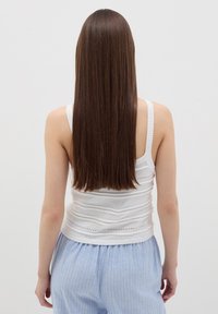 Top a maniche corte bianco lavorato a maglia con texture a coste e motivo a righe orizzontali, abbinato a pantaloni a righe blu chiaro.